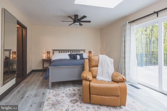 bedroom with ceiling fan, a skylight, light hardwood / wood-style flooring, and access to exterior