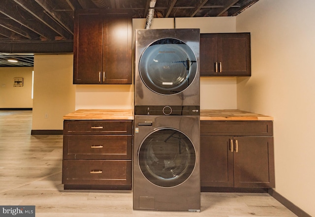 laundry room featuring stacked washing maching and dryer, cabinets, and light wood-type flooring