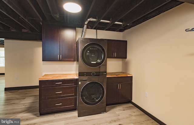 laundry area with light hardwood / wood-style flooring, stacked washing maching and dryer, and cabinets