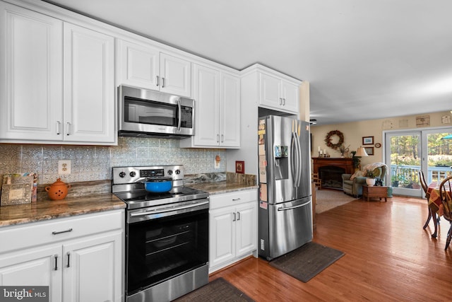 kitchen featuring tasteful backsplash, appliances with stainless steel finishes, wood-type flooring, dark stone counters, and white cabinets