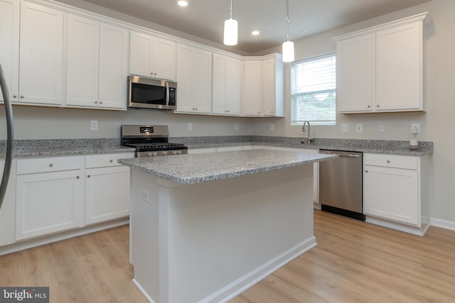 kitchen featuring light wood-type flooring, light stone counters, appliances with stainless steel finishes, a center island, and white cabinetry