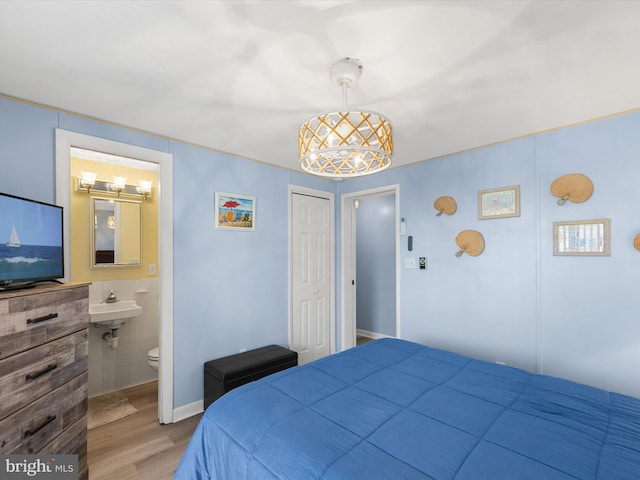 bedroom featuring tile walls, light wood-type flooring, a closet, ensuite bath, and sink