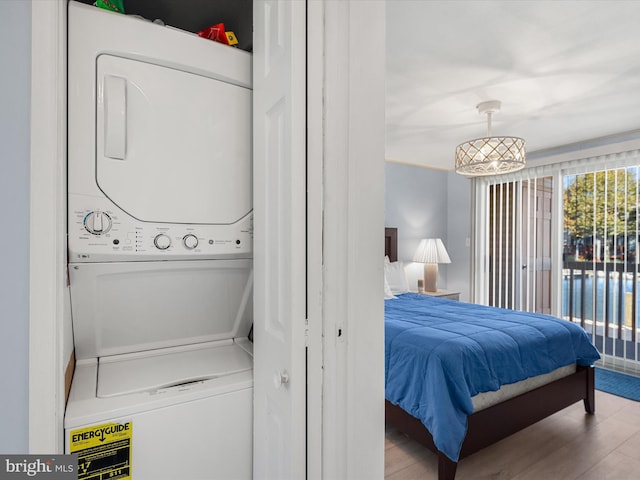 bedroom featuring a chandelier, stacked washer and clothes dryer, and light hardwood / wood-style floors