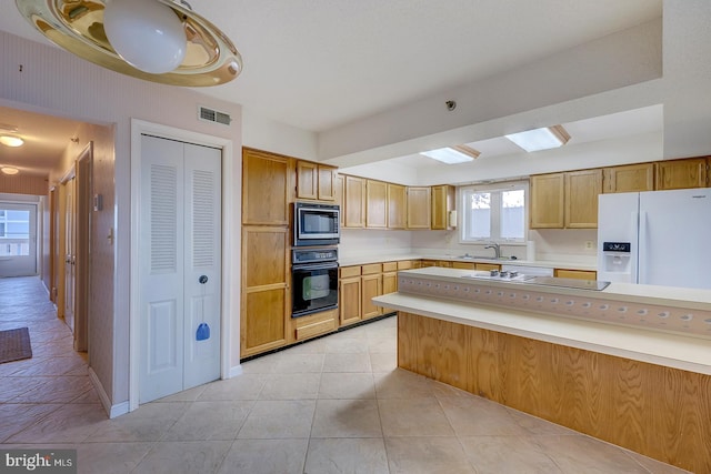 kitchen with stainless steel microwave, black oven, white fridge with ice dispenser, sink, and light tile patterned floors