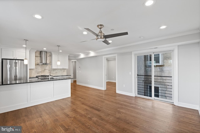 kitchen with white cabinets, stainless steel refrigerator, wall chimney exhaust hood, and pendant lighting