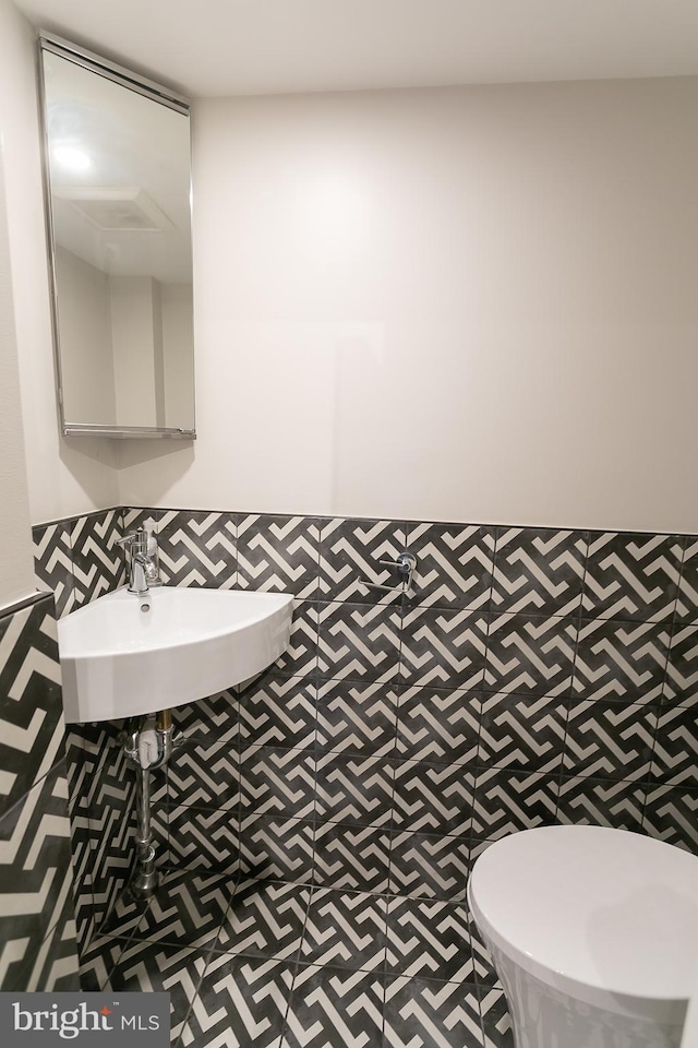 bathroom featuring toilet, sink, and tile walls