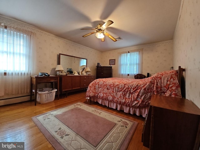 bedroom with ceiling fan, light wood-type flooring, baseboard heating, and multiple windows