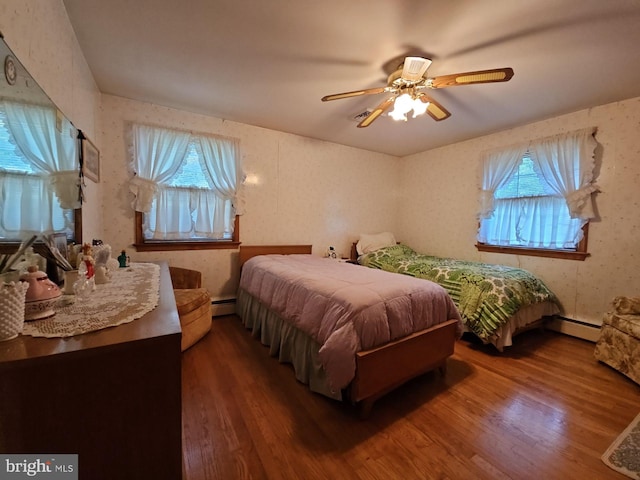 bedroom featuring ceiling fan, baseboard heating, dark hardwood / wood-style flooring, and multiple windows