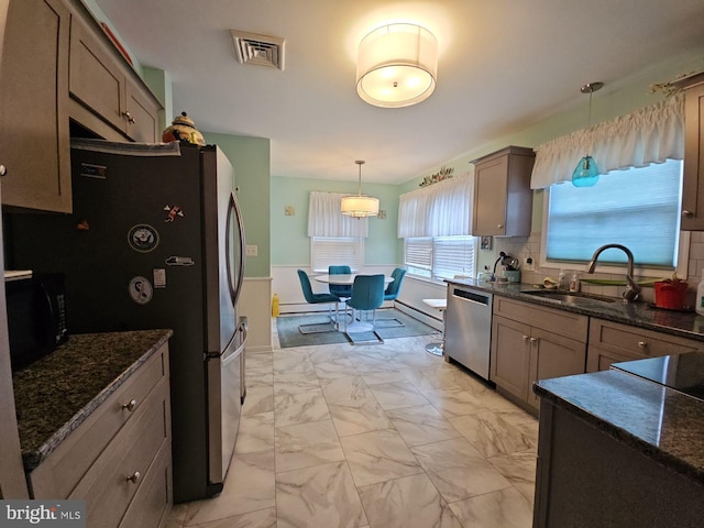 kitchen featuring sink, tasteful backsplash, decorative light fixtures, appliances with stainless steel finishes, and dark stone counters