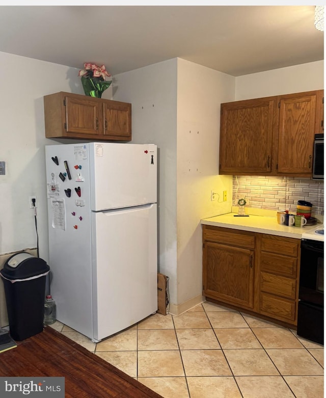 kitchen with tasteful backsplash, black electric range oven, light tile patterned floors, and white refrigerator