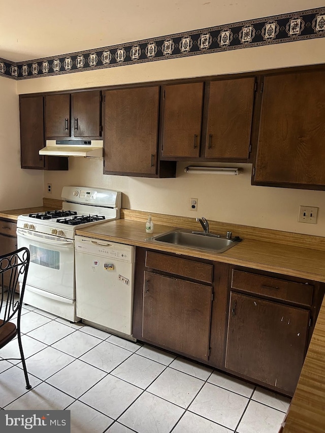 kitchen featuring white appliances, light tile patterned flooring, dark brown cabinetry, and sink