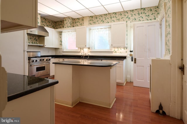 kitchen with high end stainless steel range, wood-type flooring, extractor fan, white cabinetry, and a center island