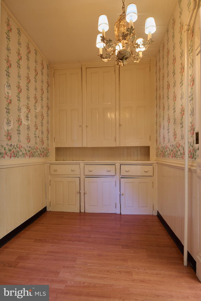 kitchen with light hardwood / wood-style floors, white cabinetry, pendant lighting, ornamental molding, and a notable chandelier