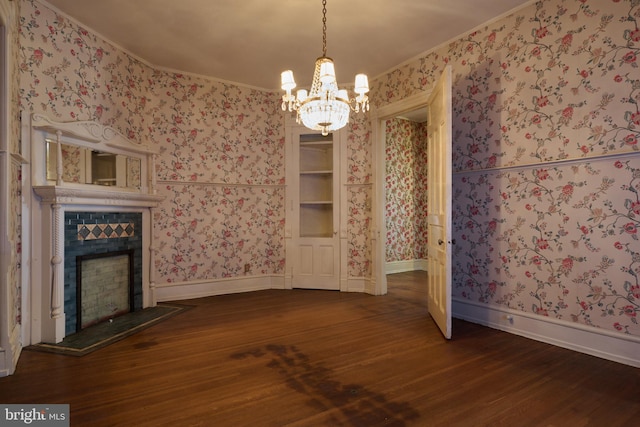 unfurnished dining area with an inviting chandelier, crown molding, dark wood-type flooring, and a tile fireplace