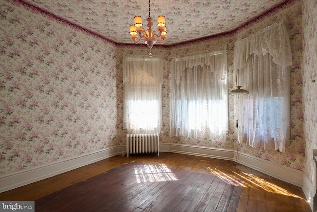 empty room with radiator heating unit, a notable chandelier, and hardwood / wood-style flooring