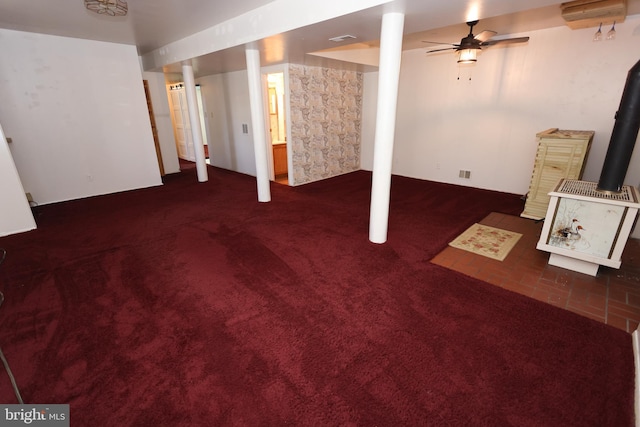 basement featuring dark colored carpet, a wood stove, and ceiling fan