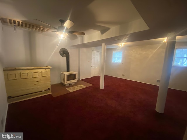 basement featuring ceiling fan, dark carpet, and a wood stove