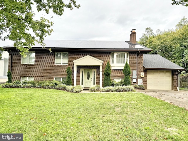 bi-level home with a garage, a chimney, brick siding, a front lawn, and driveway