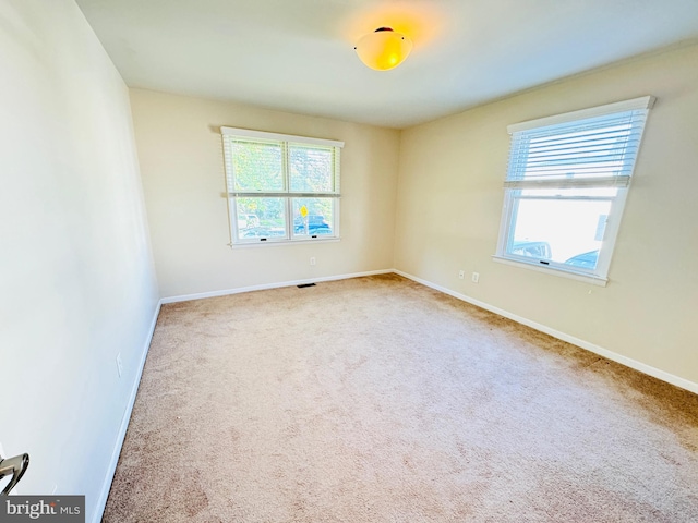 carpeted empty room featuring plenty of natural light, visible vents, and baseboards