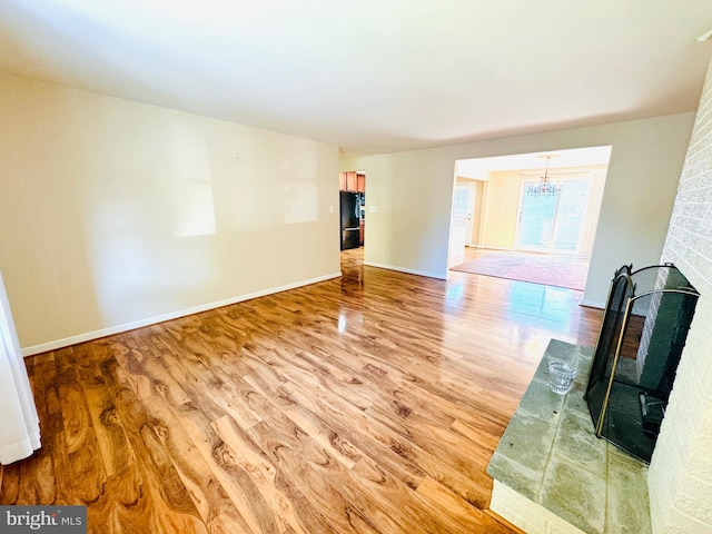 unfurnished living room featuring a chandelier, wood-type flooring, and a brick fireplace