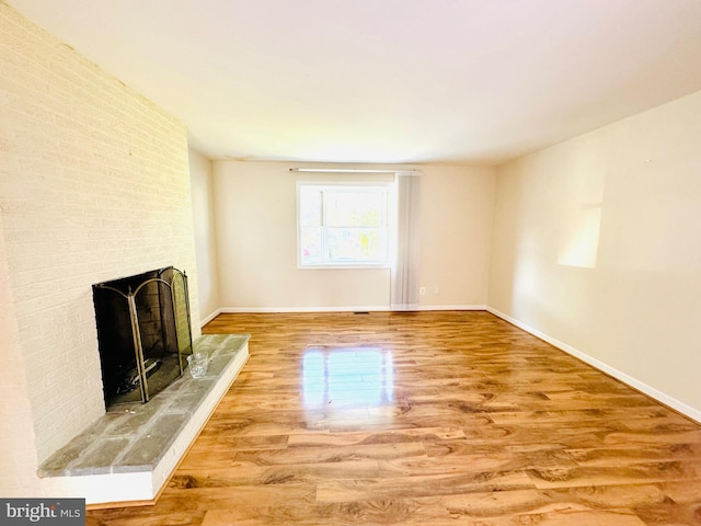 unfurnished living room with wood-type flooring and a brick fireplace