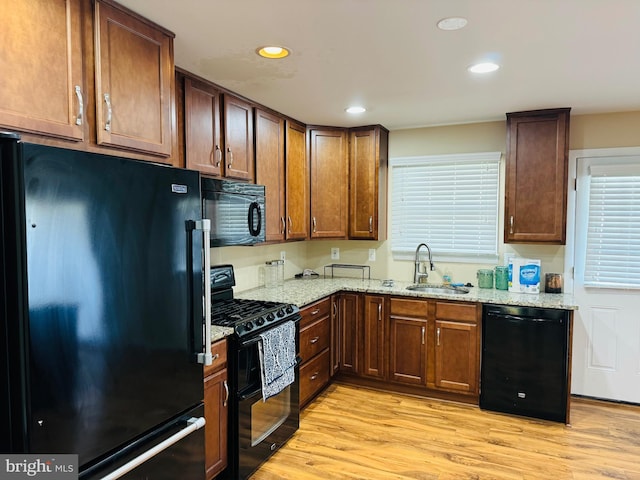 kitchen with a sink, black appliances, recessed lighting, light stone countertops, and light wood-style flooring
