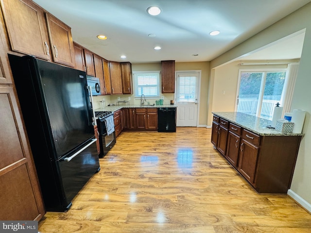 kitchen with sink, black appliances, light stone counters, and light hardwood / wood-style floors