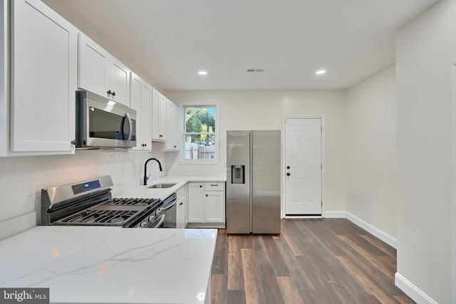 kitchen with appliances with stainless steel finishes, sink, dark hardwood / wood-style flooring, white cabinets, and light stone counters