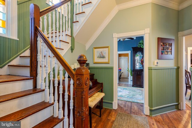 stairs featuring wood-type flooring, ornamental molding, vaulted ceiling, and a healthy amount of sunlight