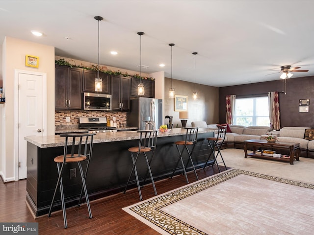 kitchen with an island with sink, stainless steel appliances, dark wood-type flooring, light stone counters, and a breakfast bar