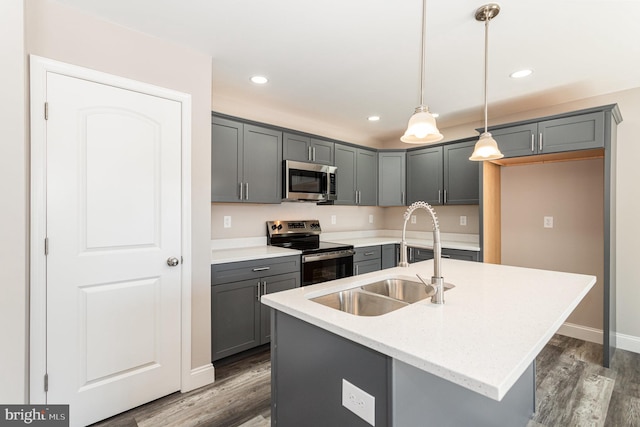 kitchen with gray cabinetry, stainless steel appliances, a kitchen island with sink, sink, and hanging light fixtures