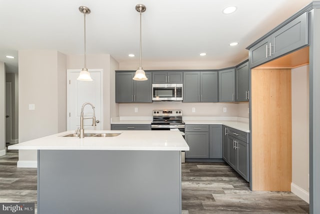 kitchen featuring appliances with stainless steel finishes, dark wood-type flooring, sink, pendant lighting, and an island with sink