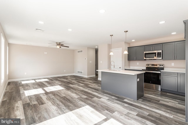 kitchen featuring appliances with stainless steel finishes, gray cabinetry, a kitchen island with sink, ceiling fan, and decorative light fixtures