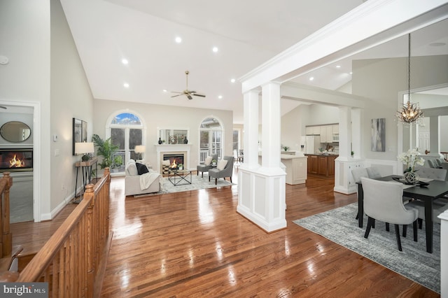 dining room featuring decorative columns, ceiling fan with notable chandelier, hardwood / wood-style floors, and high vaulted ceiling