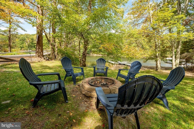 view of property's community featuring a water view, a lawn, and an outdoor fire pit