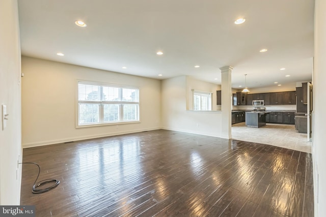 unfurnished living room featuring decorative columns and dark hardwood / wood-style flooring