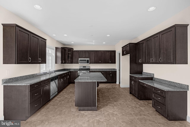 kitchen featuring sink, dark brown cabinets, appliances with stainless steel finishes, a center island, and light stone countertops