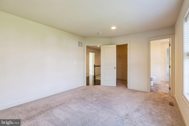 unfurnished bedroom featuring light colored carpet, a closet, ensuite bath, and a spacious closet