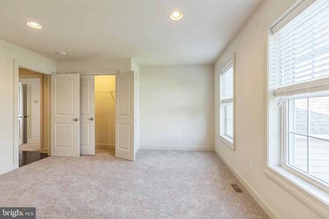 unfurnished bedroom featuring light colored carpet and a walk in closet