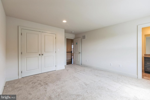 unfurnished bedroom featuring ensuite bath, a closet, and light colored carpet