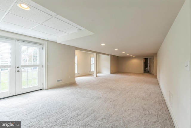 basement featuring french doors, light carpet, and a paneled ceiling