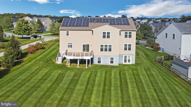 back of property with solar panels, a deck, and a lawn