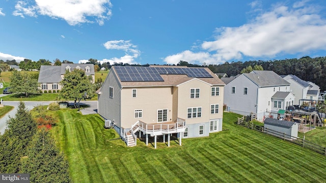 rear view of house featuring a lawn, a wooden deck, solar panels, and central AC unit