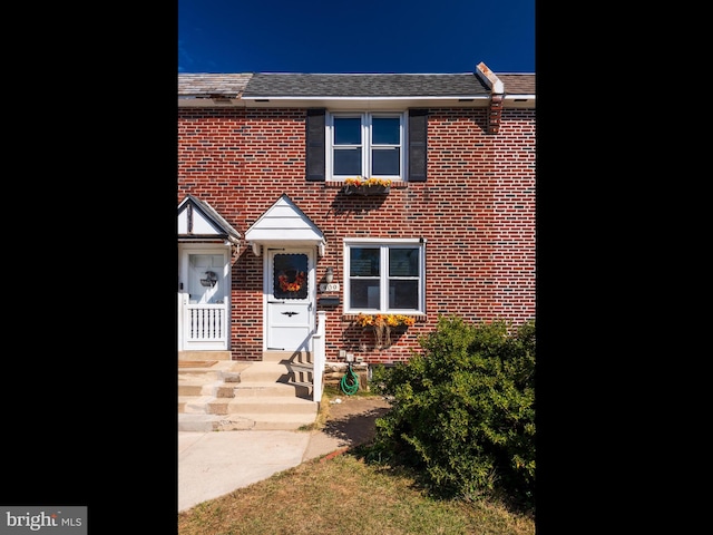 view of property featuring a shingled roof and brick siding