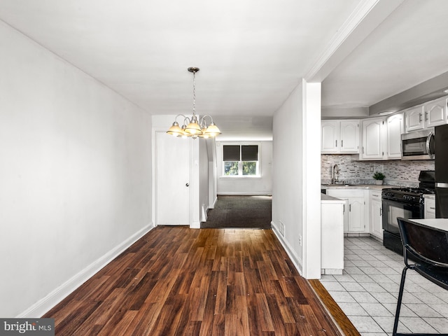 kitchen with black gas range, hardwood / wood-style floors, white cabinetry, and an inviting chandelier