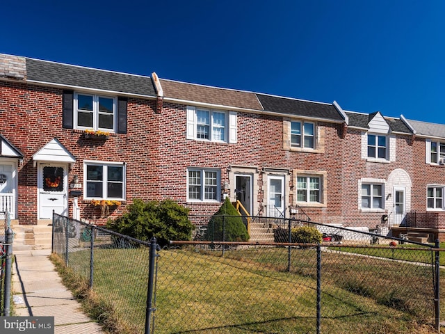 view of property with brick siding, fence, a front lawn, and roof with shingles