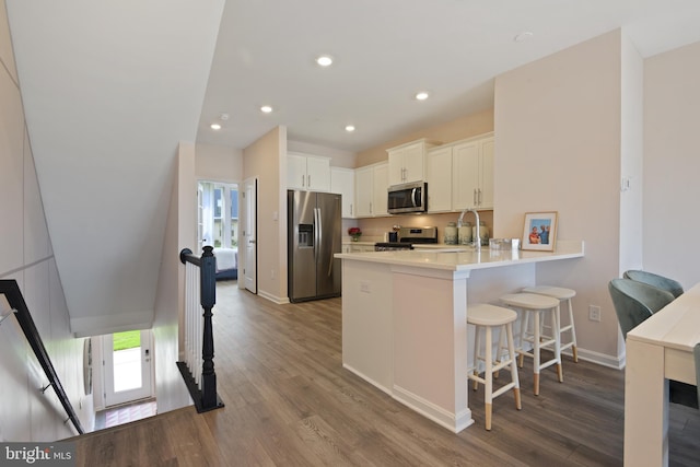 kitchen with hardwood / wood-style flooring, kitchen peninsula, a breakfast bar area, white cabinetry, and appliances with stainless steel finishes