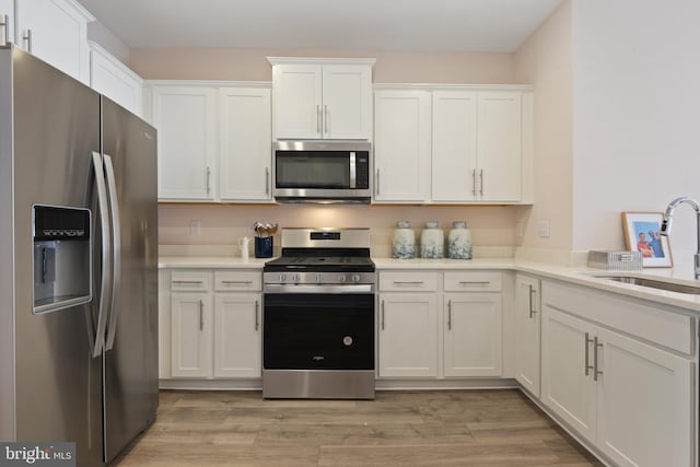 kitchen with appliances with stainless steel finishes, white cabinetry, sink, and light hardwood / wood-style floors