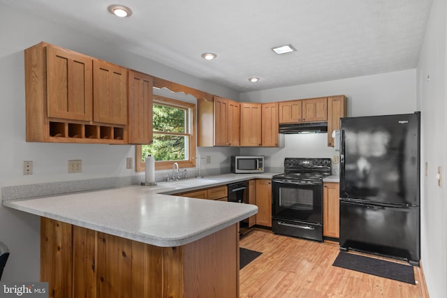 kitchen with sink, light wood-type flooring, kitchen peninsula, and black appliances