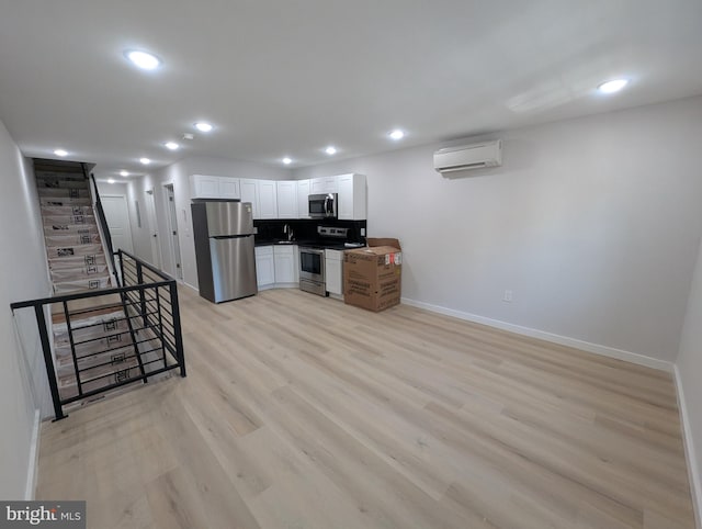 kitchen with stainless steel appliances, a wall mounted air conditioner, white cabinets, and baseboards